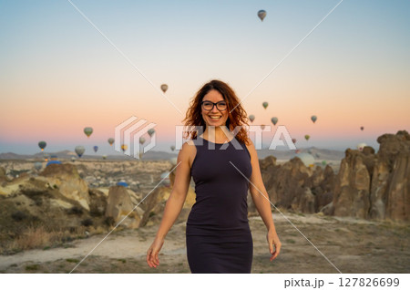 Caucasian woman posing against the backdrop of balloons flying over Cappadocia at sunrise.  127826699
