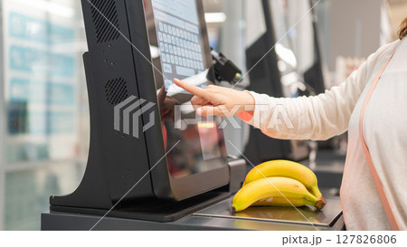 Faceless woman using self-checkout technology at grocery store. Faceless woman using self-checkout technology at grocery store. 127826806