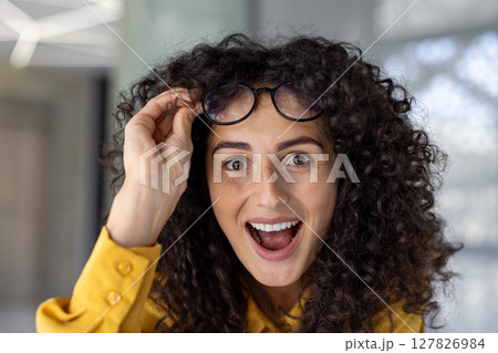 Hispanic businesswoman showcasing surprise and excitement in office, lifting glasses with cheerful expression. Captures moment of joy and enthusiasm in professional environment. Hispanic businesswoman showcasing surprise and excitement in office, lifting glasses with cheerful expression. Captures moment of joy and enthusiasm in professional environment. 127826984