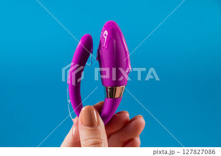 A woman holds a curved sex toy in lubrication on a blue background. Vaginally clitoral vibrator.  127827086