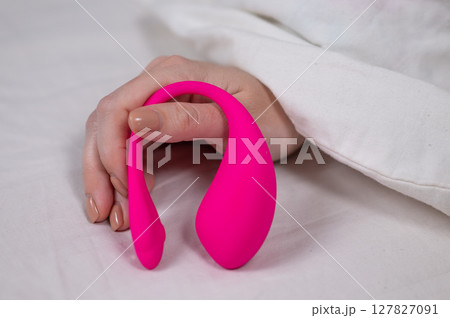 Woman holding curved pink vibrator while lying in bed.  127827091