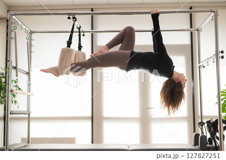 Caucasian woman doing aerial exercises on a reformer machine. Caucasian woman doing aerial exercises on a reformer machine. 127827251
