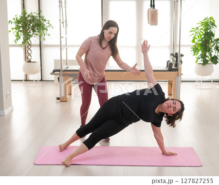 Overweight caucasian woman doing pilates exercises with personal trainer. Overweight caucasian woman doing pilates exercises with personal trainer. 127827255