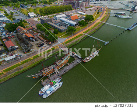 An aerial view of a coastal town with a harbor, colorful buildings and a replica ship docked along the water. Surrounding areas include parking lots and green spaces. 127827333