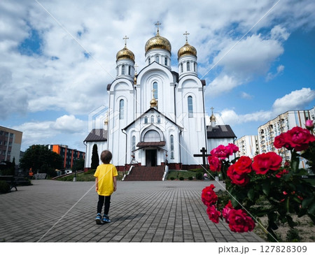Child in yellow T-shirt is standing in front of Orthodox church in summer. View from back. Golden domes. Church on sunny day. child in front of the church. 127828309