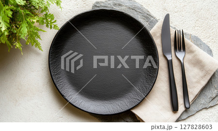 Ultra realistic empty black matte plate on slate-grey stone surface with fork and knife on linen napkin. Clean and bright kitchen background 127828603