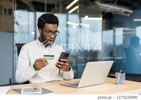 Upset disappointed man with phone in hands and bank credit card. Businessman got account blocked, fraudulent actions deception at workplace inside office. 127828990