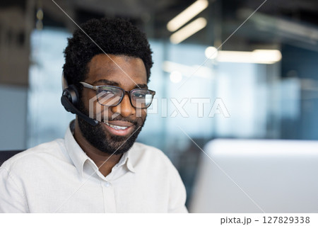 Portrait of a support worker, a man with a headset smiling and looking at the camera. A company employee close-up with a laptop inside the office 127829338