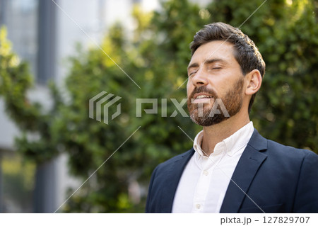 A relaxed man in a suit enjoys the outdoors, eyes closed, appearing content and at peace with nature. A relaxed man in a suit enjoys the outdoors, eyes closed, appearing content and at peace with nature. 127829707
