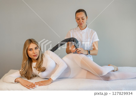 Woman in special white suit getting anti cellulite massage in a spa salon. LPG, and body contouring treatment in clinic.Reset body weight with LPG massage.  127829934