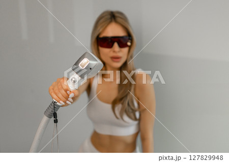 Woman tunes a laser hair removal machine. She holds a working part of the epilator in her hands and poses for a photo. Body Care. Underarm Laser Hair Removal. 127829948