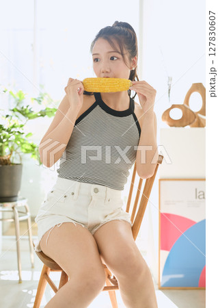 部屋でとうもろこしを手に笑顔を見せる若い女性 127830607