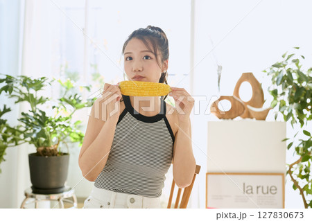 部屋でとうもろこしを手に笑顔を見せる若い女性 127830673