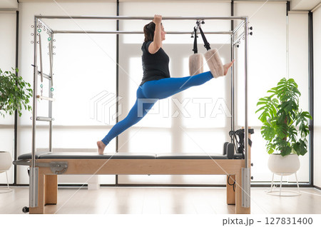Focused Woman Practicing Pilates on a Reformer. Focused Woman Practicing Pilates on a Reformer. 127831400