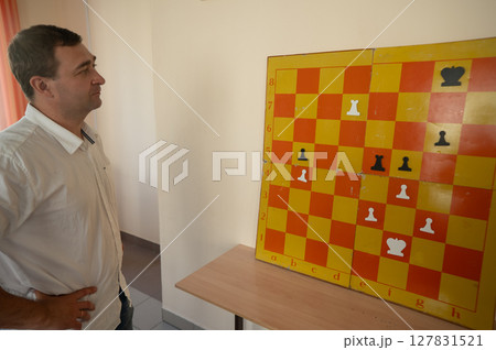 Caucasian man standing at wall mounted magnetic chessboard demonstration.  127831521