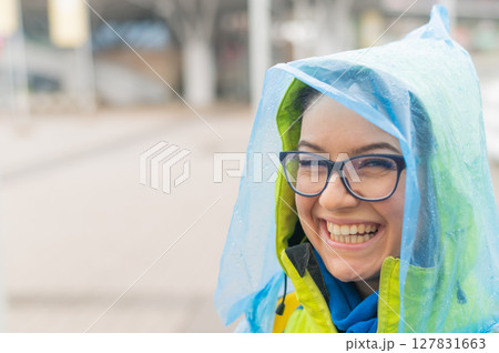 Portrait of a smiling woman with glasses wearing a raincoat outdoors. 127831663