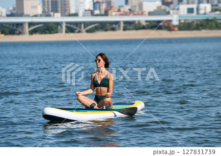 Caucasian woman doing yoga on a SUP board. Caucasian woman doing yoga on a SUP board. 127831739