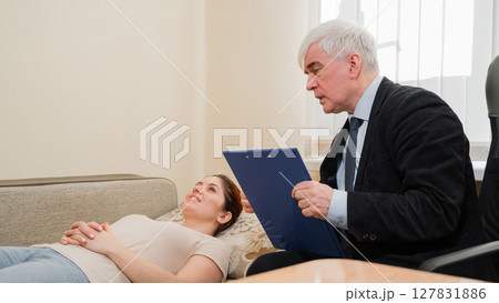 Caucasian woman lies on a couch at a reception with a psychotherapist. An elderly man works as a psychiatrist 127831886