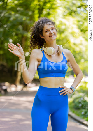 Athletic fit slim runner woman waving hi hello with hand greeting with hospitable friendly smile 127833200