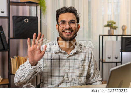 Indian business man employee waves hand hi greeting welcomes someone online webinar conversation 127833211