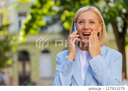 Happy mature Caucasian businesswoman lady smiling laughs while talking on smartphone on city street Happy mature Caucasian businesswoman lady smiling laughs while talking on smartphone on city street 127833279