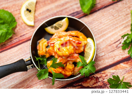 Juicy fried shrimps with lemon wedges in a frying pan on a wooden 127833441