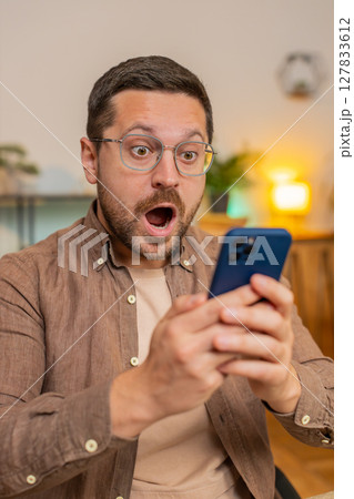 Caucasian young man guy using smartphone shocked by sudden victory sitting in home office room 127833612