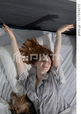 Woman Enjoying a Lazy Morning in Bed With a Cozy Atmosphere and Pet Dog Nearby 127834272