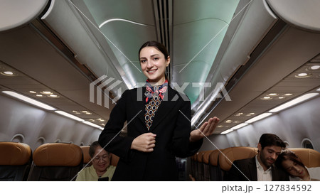 Smiling flight attendant in uniform welcomes and guides passengers aboard a modern airplane. Smiling flight attendant in uniform welcomes and guides passengers aboard a modern airplane. 127834592