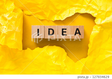 Crumpled yellow paper framing wooden cubes spelling idea on yellow background Crumpled yellow paper framing wooden cubes spelling idea on yellow background 127834629