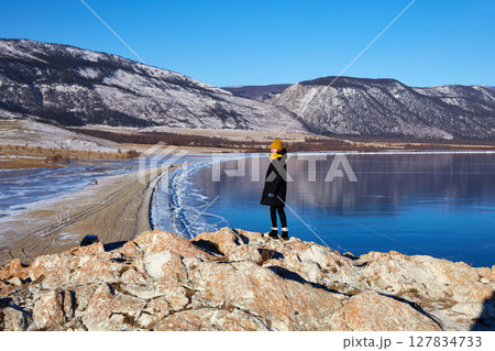 A happy young girl is traveling on Lake Baikal in winter. Beautiful winter mountain landscape, transparent ice. 127834733