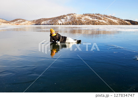 A happy girl lies on the ice of the frozen Lake Baikal. 127834747