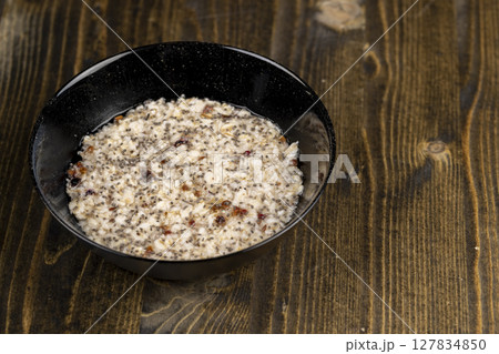 boiled oatmeal porridge with dried berries and fruits in a black bowl , cooking instant oatmeal porridge, chia in porridge, top view 127834850