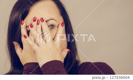 Woman peeking through her hands 127836004