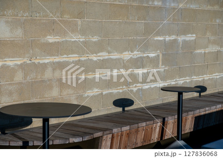 Wooden seating and metal tables next to the concrete wall 127836068