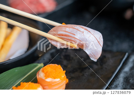 Chopsticks holding salmon sushi, in the restaurant 127836079