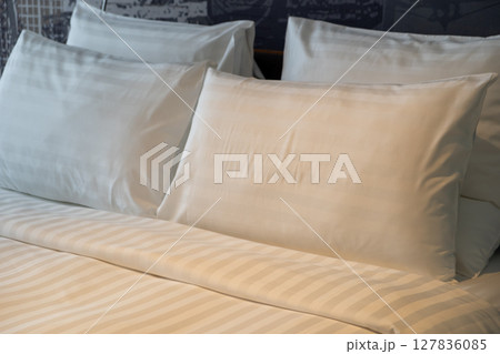 A neatly made hotel bed with soft pillows with warm reading light 127836085