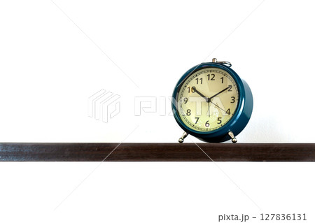 Vintage blue alarm clock displaying time at 10:10 placed on dark wooden shelf with clean white background Vintage blue alarm clock displaying time at 10:10 placed on dark wooden shelf with clean white background 127836131