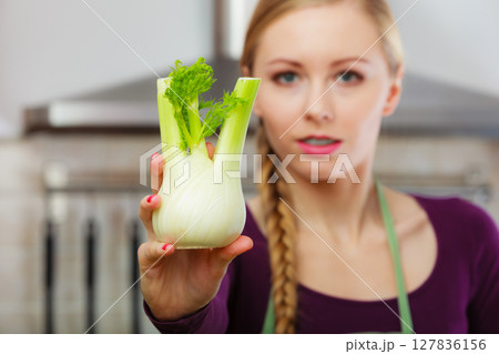 Woman in kitchen holds raw fennel bulb vegetable 127836156