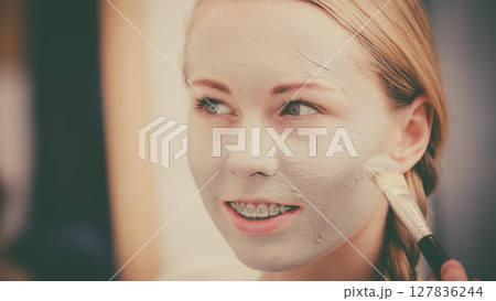Woman applying with brush clay mud mask to her face 127836244