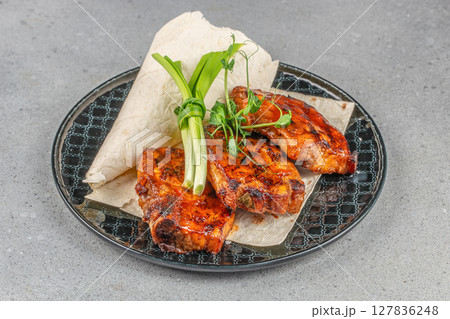 Grilled barbecue pork ribs served with fresh green onions and flatbread on a decorative black ceramic plate Grilled barbecue pork ribs served with fresh green onions and flatbread on a decorative black ceramic plate 127836248