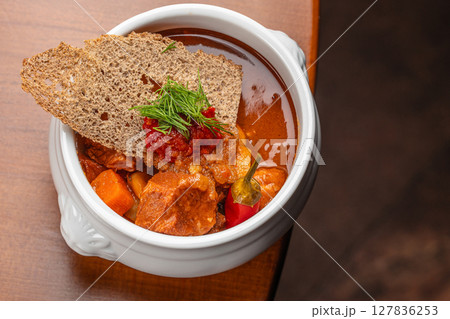 Hearty beef stew with vegetables, chili pepper, and rye crisps served in a ceramic bowl, garnished with dill and spicy tomato relish Hearty beef stew with vegetables, chili pepper, and rye crisps served in a ceramic bowl, garnished with dill and spicy tomato relish 127836253
