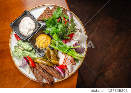 A rustic appetizer platter featuring rye bread, pickles, mustard, creamy dips, herbs, onion slices, green onion, lard, and fresh vegetables arranged for traditional Eastern European dining A rustic appetizer platter featuring rye bread, pickles, mustard, creamy dips, herbs, onion slices, green onion, lard, and fresh vegetables arranged for traditional Eastern European dining 127836261
