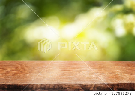 A smooth wooden tabletop set against a bright, sun-dappled green background, perfect for showcasing natural products or summer-themed content 127836278