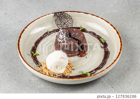 A rich molten chocolate lava cake with a scoop of vanilla ice cream, garnished with chocolate sauce, cookie crumbs, mint leaves, and powdered sugar 127836286