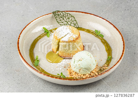 A golden matcha lava cake with powdered sugar and green tea sauce served alongside a scoop of mint ice cream and crumbled nuts, elegantly garnished with fresh mint. 127836287