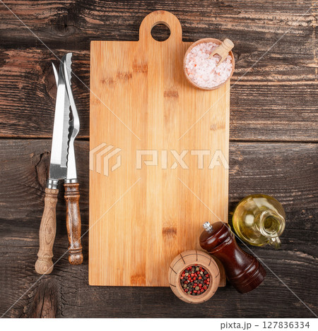 A rustic wooden cutting board surrounded by vintage kitchen utensils, spices, and olive oil on a dark wooden table, perfect for cooking or recipe background concepts 127836334