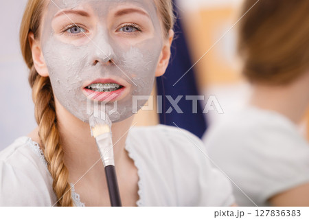 Happy young woman applying mud mask on face 127836383