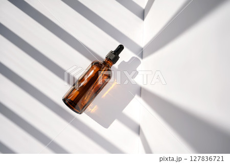 A bottle of serum made of brown glass on a white background with stripes of light. A bottle of serum made of brown glass on a white background with stripes of light. 127836721