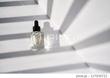 A bottle with a pipette with serum oil on a background with stripes of shadows. A bottle with a pipette with serum oil on a background with stripes of shadows. 127836722
